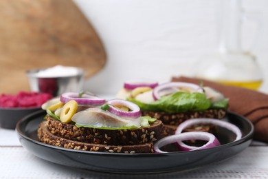 Photo of Tasty sandwiches with herring, onions, lettuce and olives on white wooden table, closeup