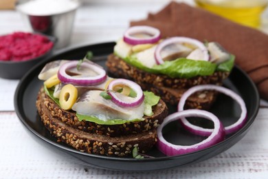 Tasty sandwiches with herring, onions, lettuce and olives on white wooden table, closeup