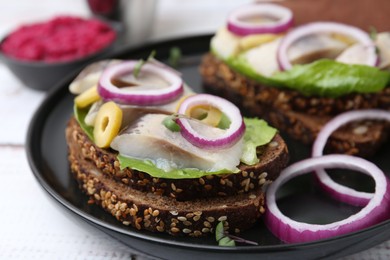 Photo of Tasty sandwiches with herring, onions, lettuce and olives on table, closeup