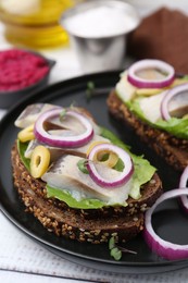 Tasty sandwiches with herring, onions, lettuce and olives on white wooden table, closeup