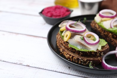 Tasty sandwiches with herring, onions, lettuce and olives on white wooden table, closeup. Space for text