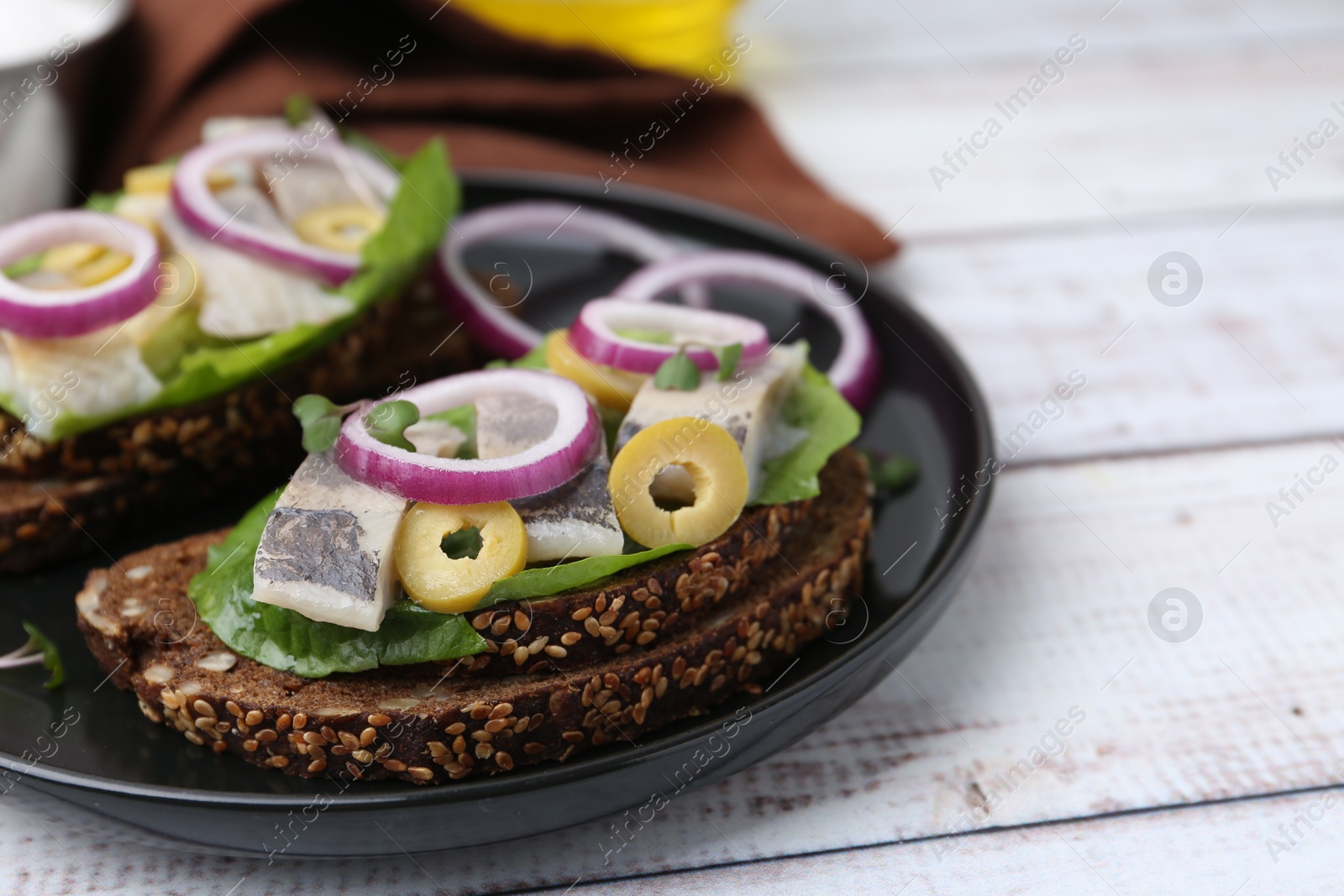 Photo of Tasty sandwiches with herring, onions, lettuce and olives on white wooden table, closeup. Space for text