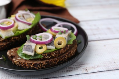 Tasty sandwiches with herring, onions, lettuce and olives on white wooden table, closeup. Space for text