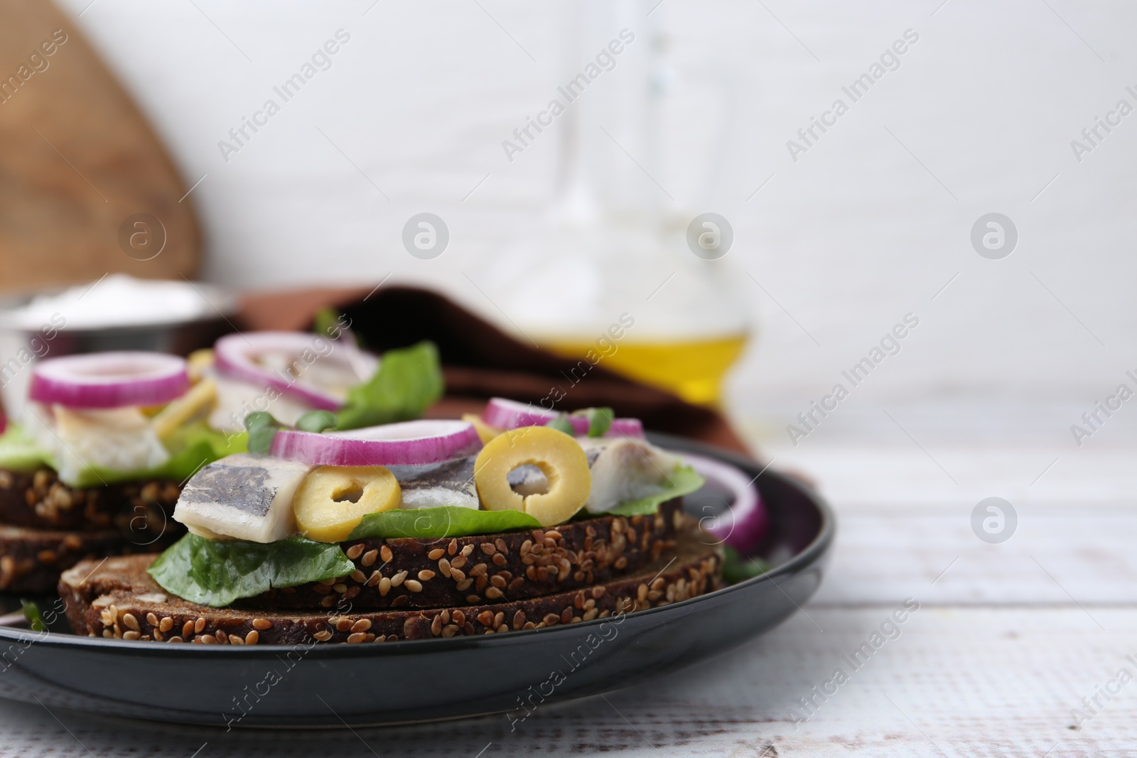 Photo of Tasty sandwiches with herring, onions, lettuce and olives on white wooden table, closeup. Space for text