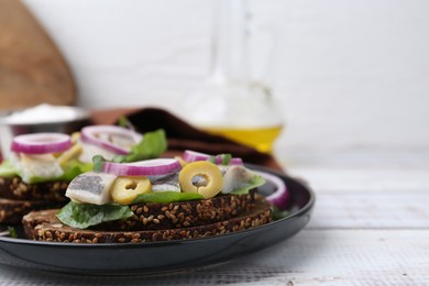 Tasty sandwiches with herring, onions, lettuce and olives on white wooden table, closeup. Space for text