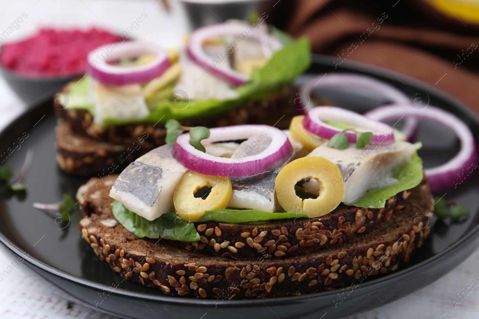 Photo of Tasty sandwiches with herring, onions, lettuce and olives on table, closeup