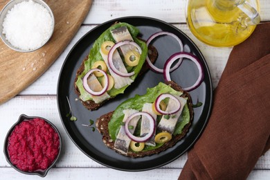 Tasty sandwiches with herring served on white wooden table, flat lay