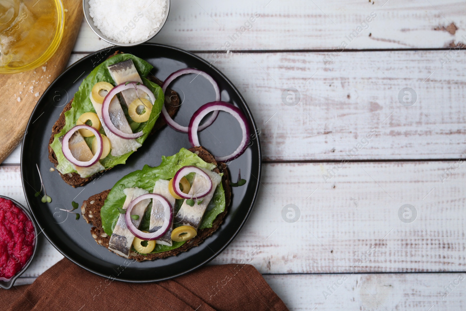 Photo of Tasty sandwiches with herring served on white wooden table, flat lay. Space for text