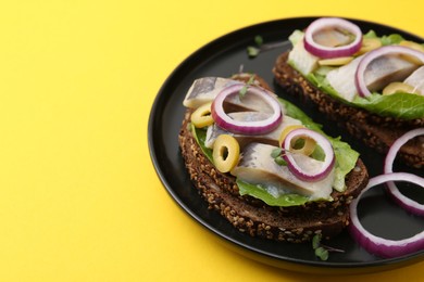 Tasty sandwiches with herring, onions, lettuce and olives on yellow background, closeup. Space for text