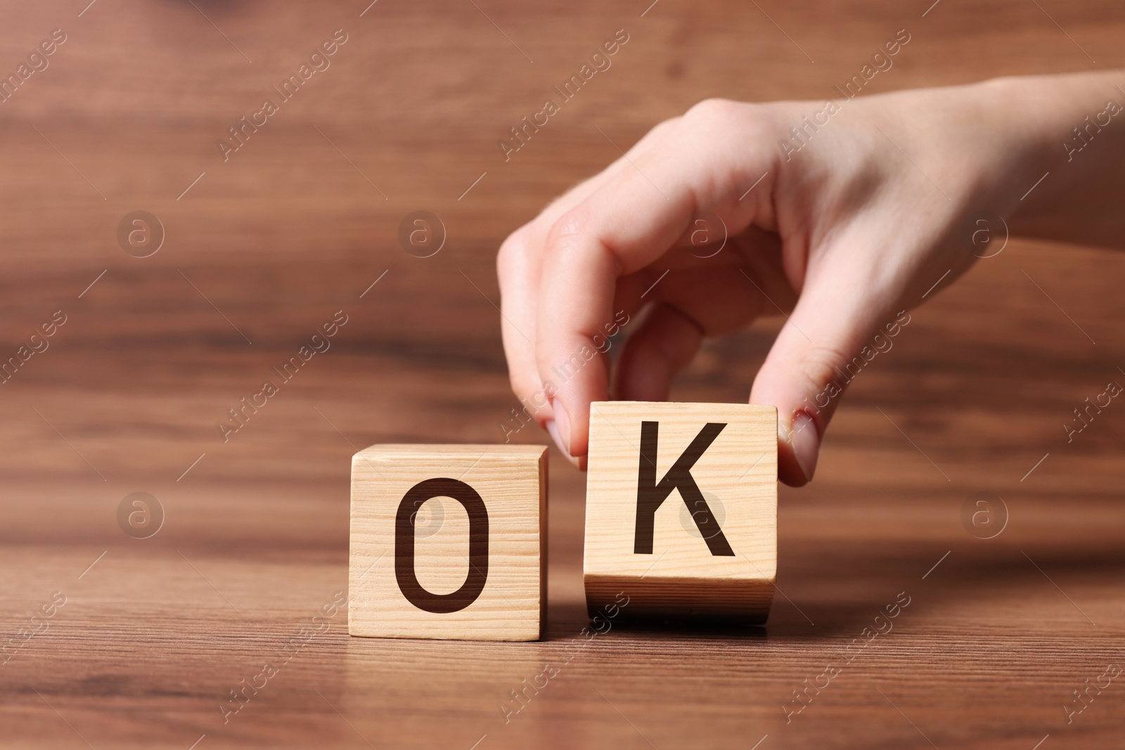 Image of Woman making abbreviation OK with cubes on wooden background, closeup