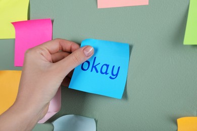 Woman sticking note with word Okay on color wall, closeup