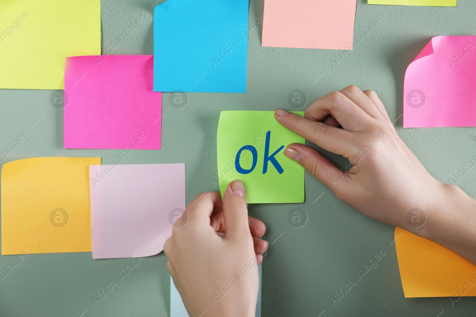 Image of Woman sticking note with abbreviation OK on color wall, closeup