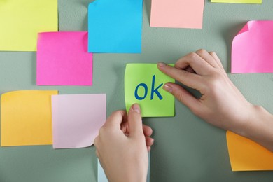 Woman sticking note with abbreviation OK on color wall, closeup