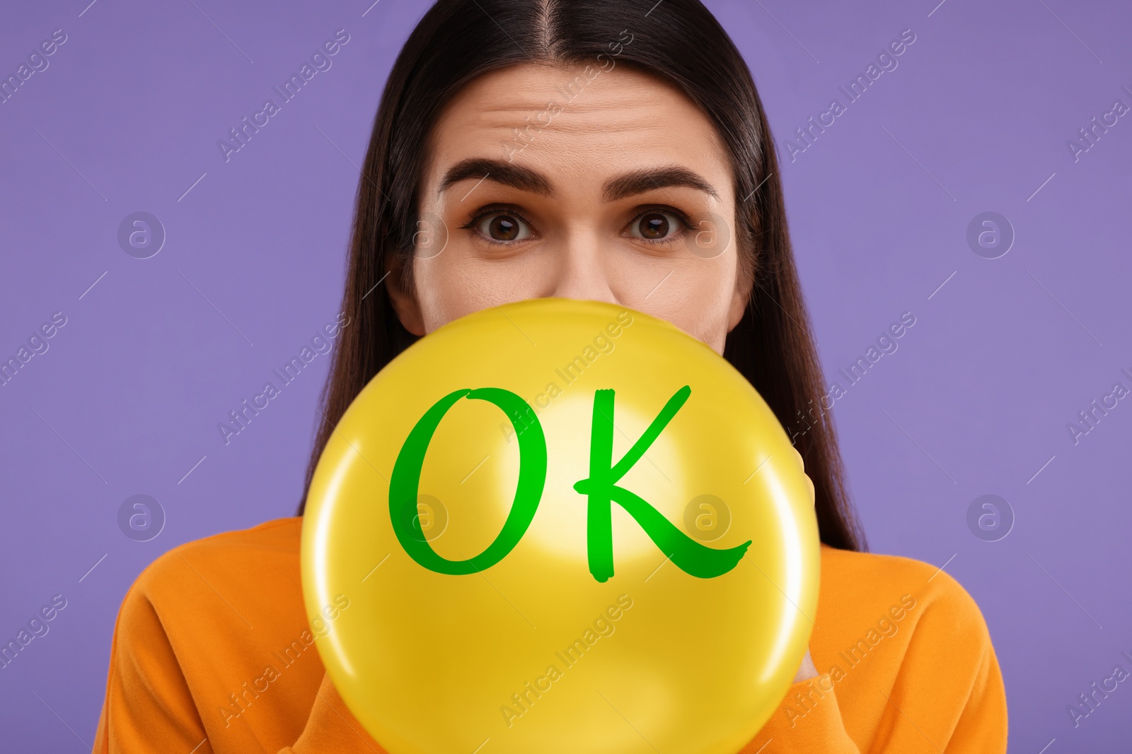 Image of Woman inflating yellow balloon with abbreviation OK on purple background