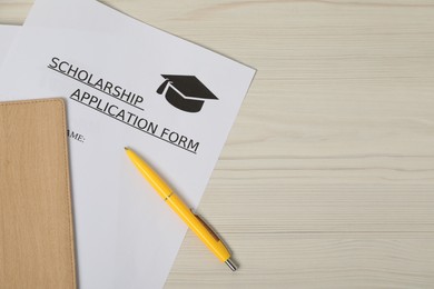 Photo of Scholarship application form and pen on wooden table, flat lay. Space for text