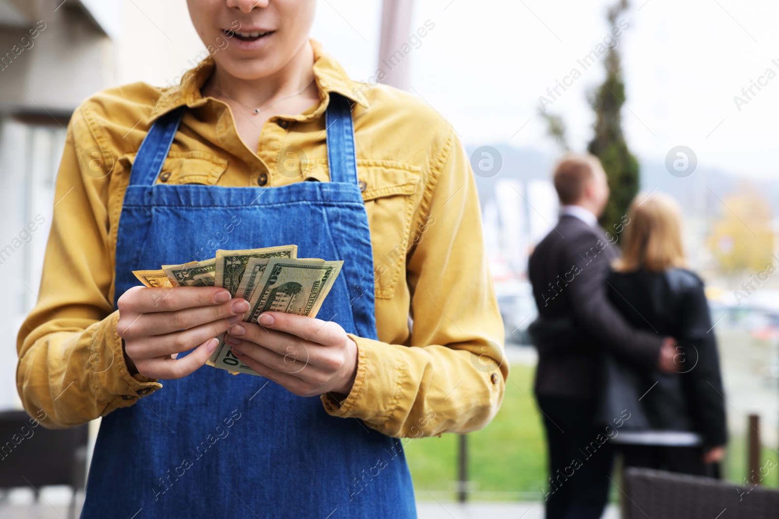 Photo of Happy waitress holding tips in outdoor cafe, closeup