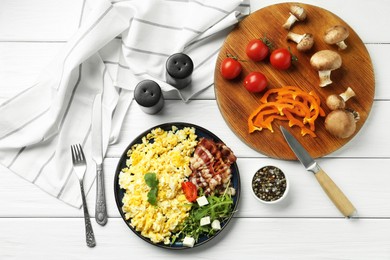 Photo of Tasty brunch. Delicious scrambled eggs, bacon and salad served on white wooden table, flat lay