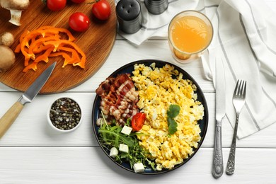 Photo of Tasty brunch. Delicious scrambled eggs, bacon, salad and glass of juice served on white wooden table, flat lay