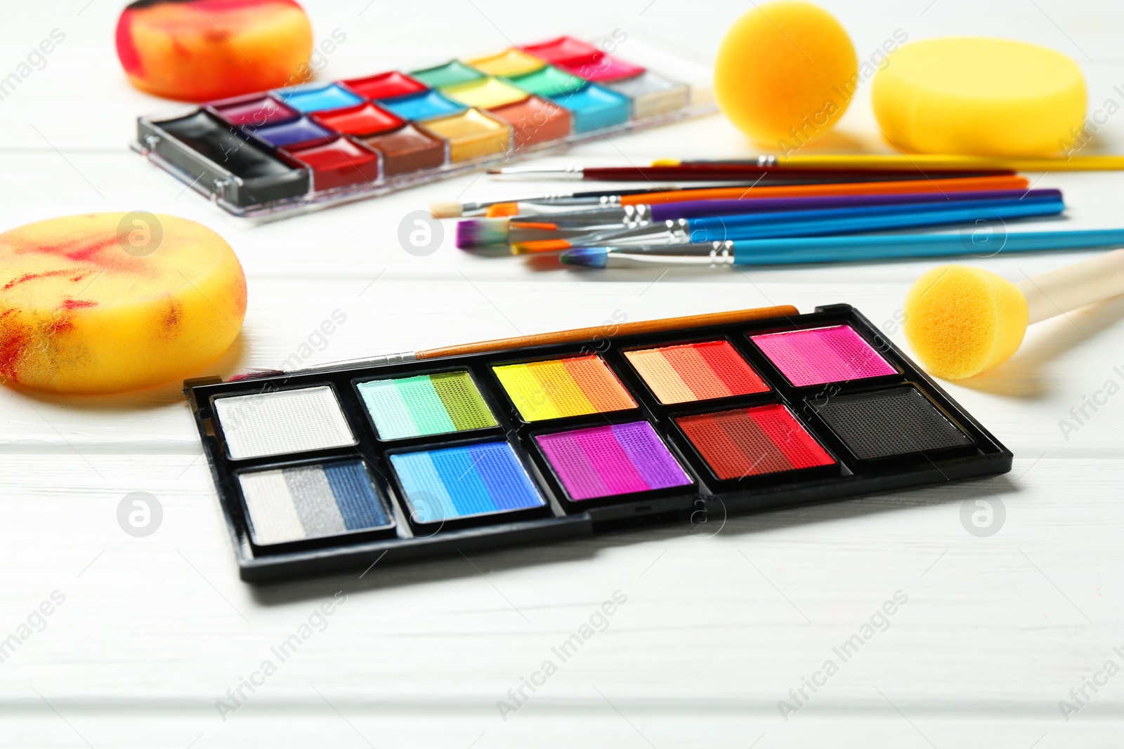 Photo of Face paints and tools on white wooden background, closeup