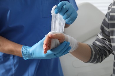 Doctor bandaging patient's hand in clinic, closeup