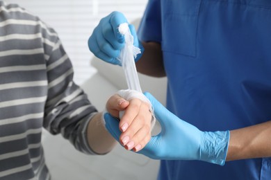 Doctor bandaging patient's hand in clinic, closeup