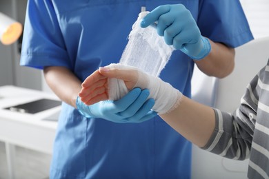 Doctor bandaging patient's hand in clinic, closeup