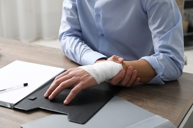 Man with medical bandage on his wrist at wooden table indoors, closeup