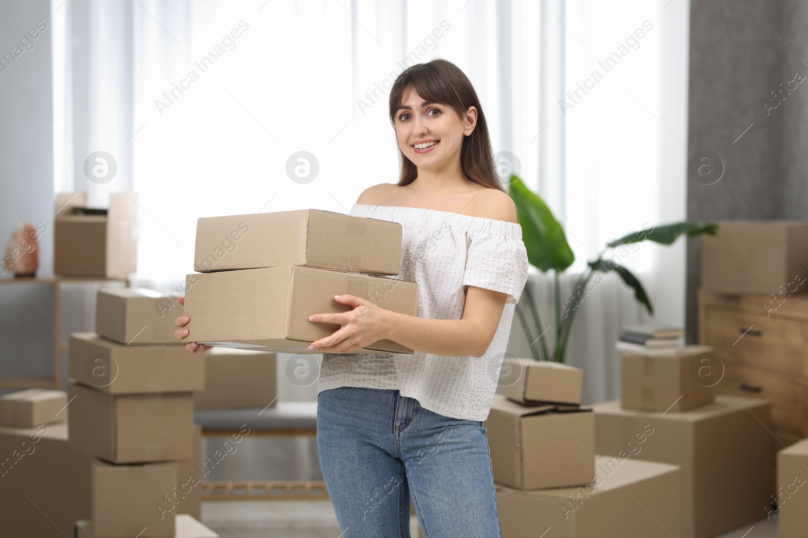 Photo of Moving day. Happy woman with cardboard boxes in her new home