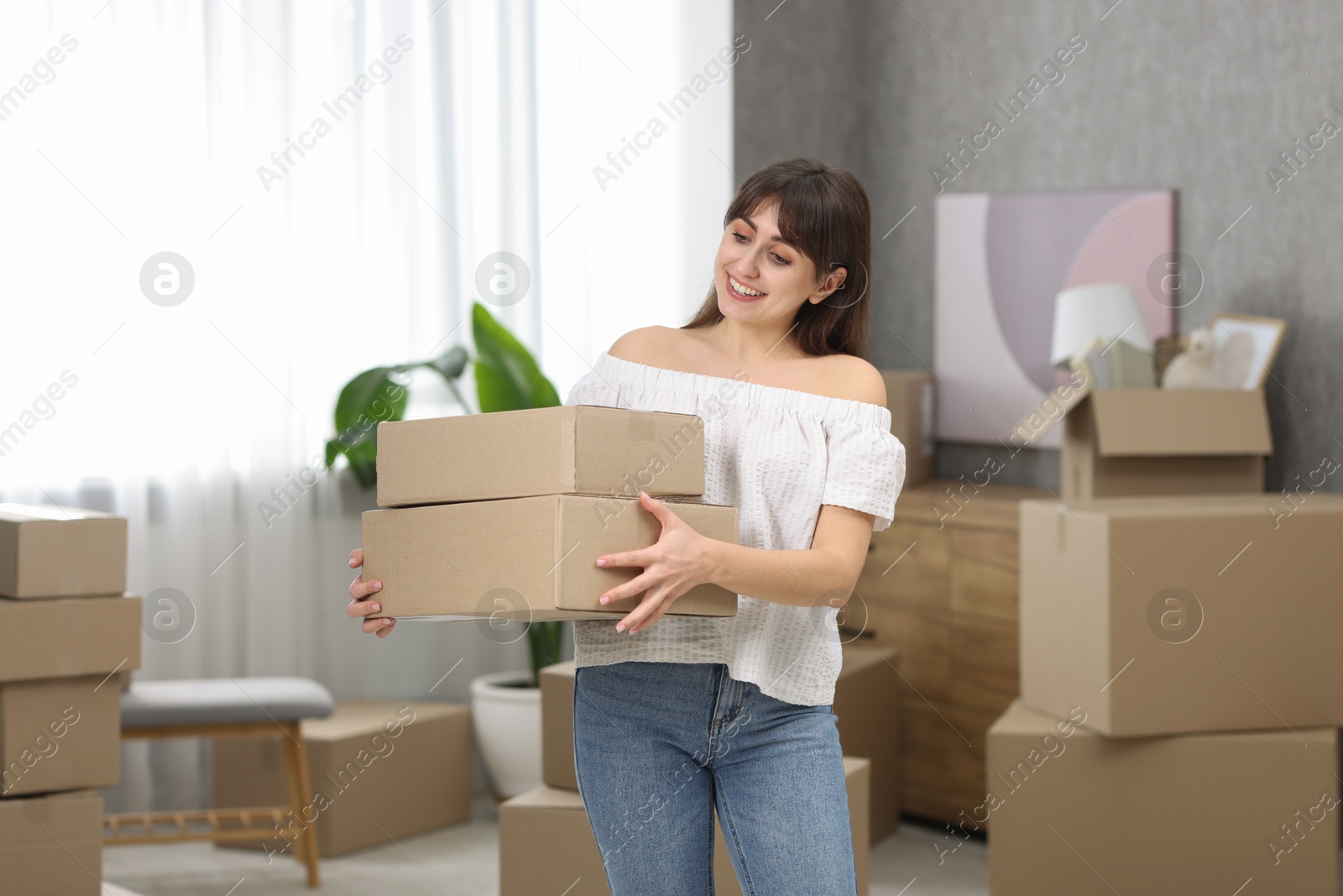 Photo of Moving day. Happy woman with cardboard boxes in her new home