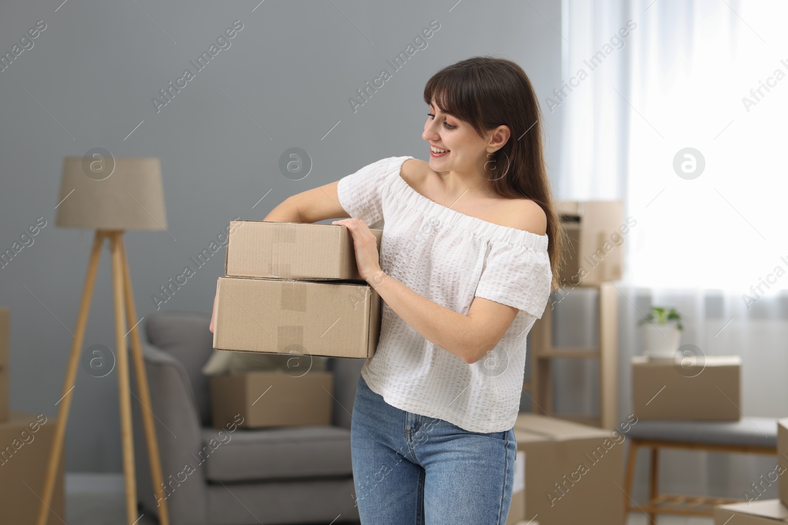 Photo of Moving day. Happy woman with cardboard boxes in her new home