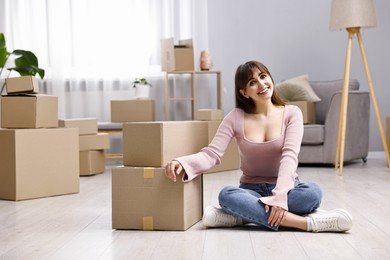 Photo of Moving day. Happy woman sitting on floor near cardboard boxes in her new home