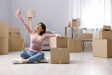 Photo of Moving day. Happy woman sitting on floor near cardboard boxes in her new home