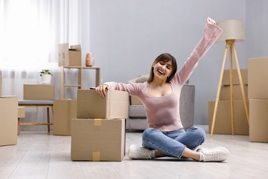 Moving day. Happy woman sitting on floor near cardboard boxes in her new home