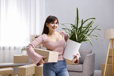 Moving day. Happy woman with cardboard box and houseplant in her new home