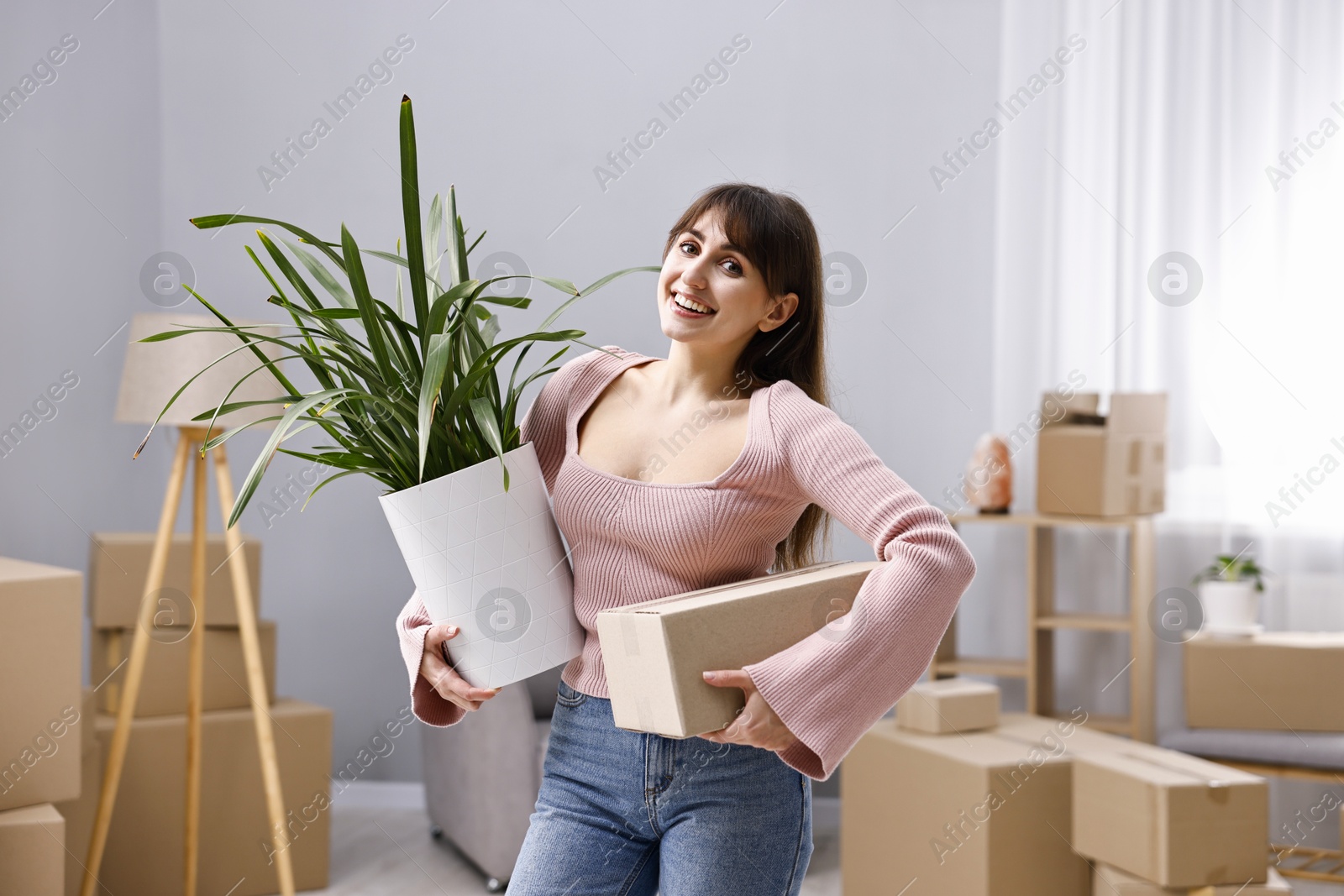 Photo of Moving day. Happy woman with cardboard box and houseplant in her new home