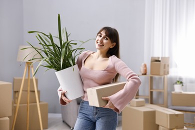 Moving day. Happy woman with cardboard box and houseplant in her new home