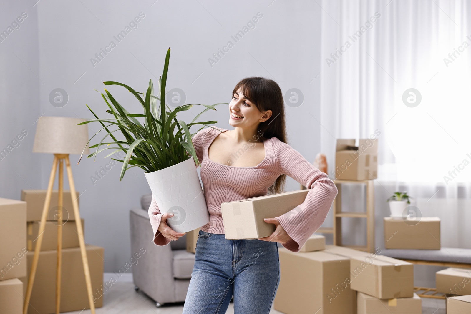 Photo of Moving day. Happy woman with cardboard box and houseplant in her new home