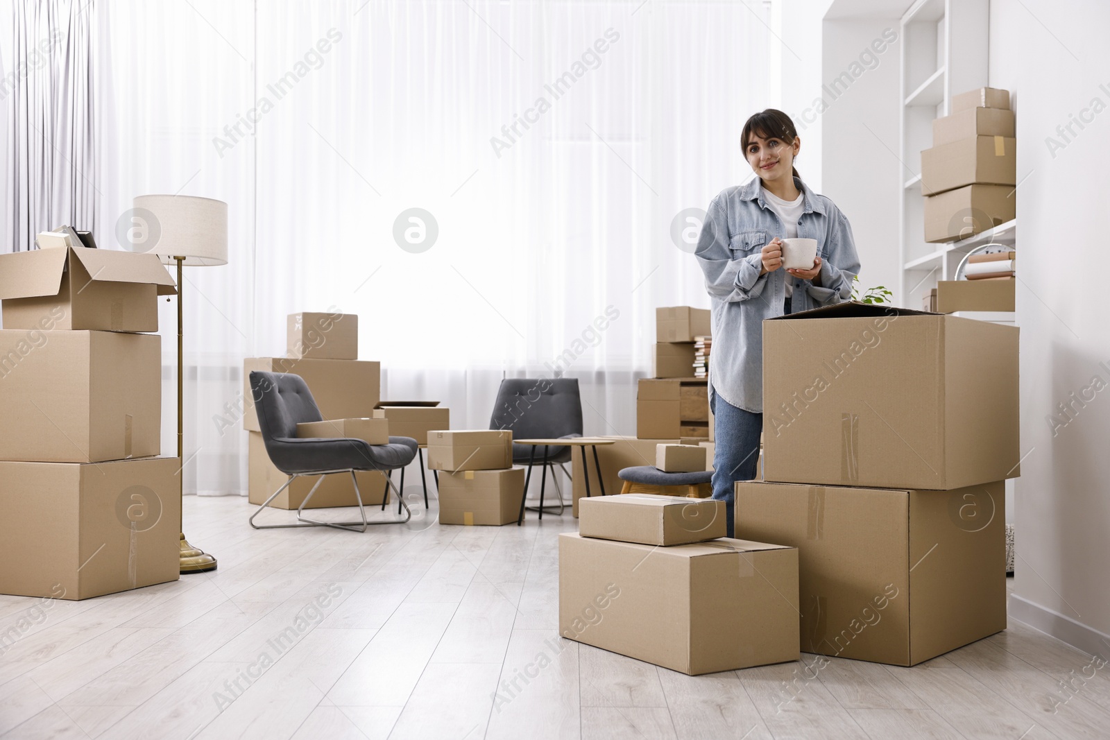 Photo of Moving day. Woman with cup of drink and cardboard boxes in her new home