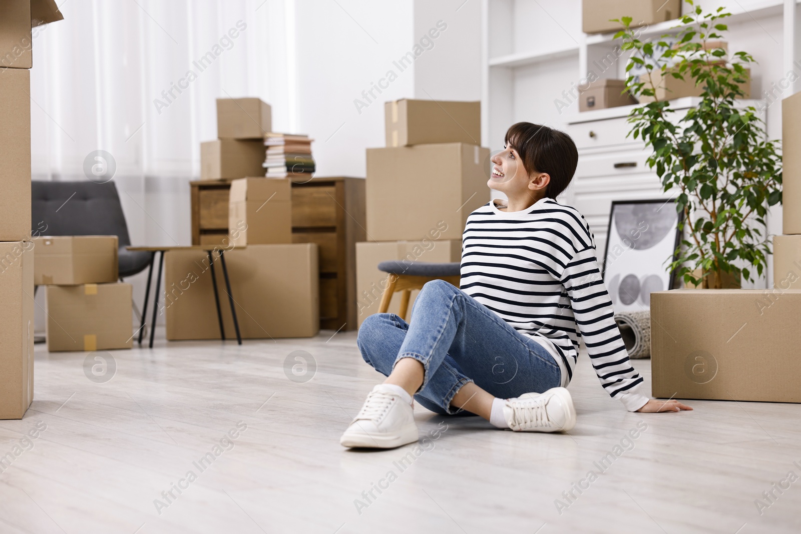 Photo of Moving day. Happy woman resting on floor and cardboard boxes in her new home