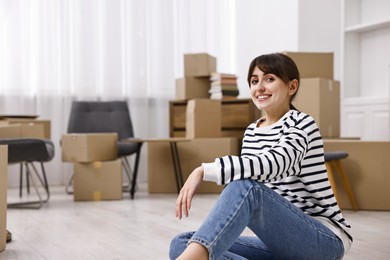 Photo of Moving day. Happy woman resting on floor and cardboard boxes in her new home, space for text