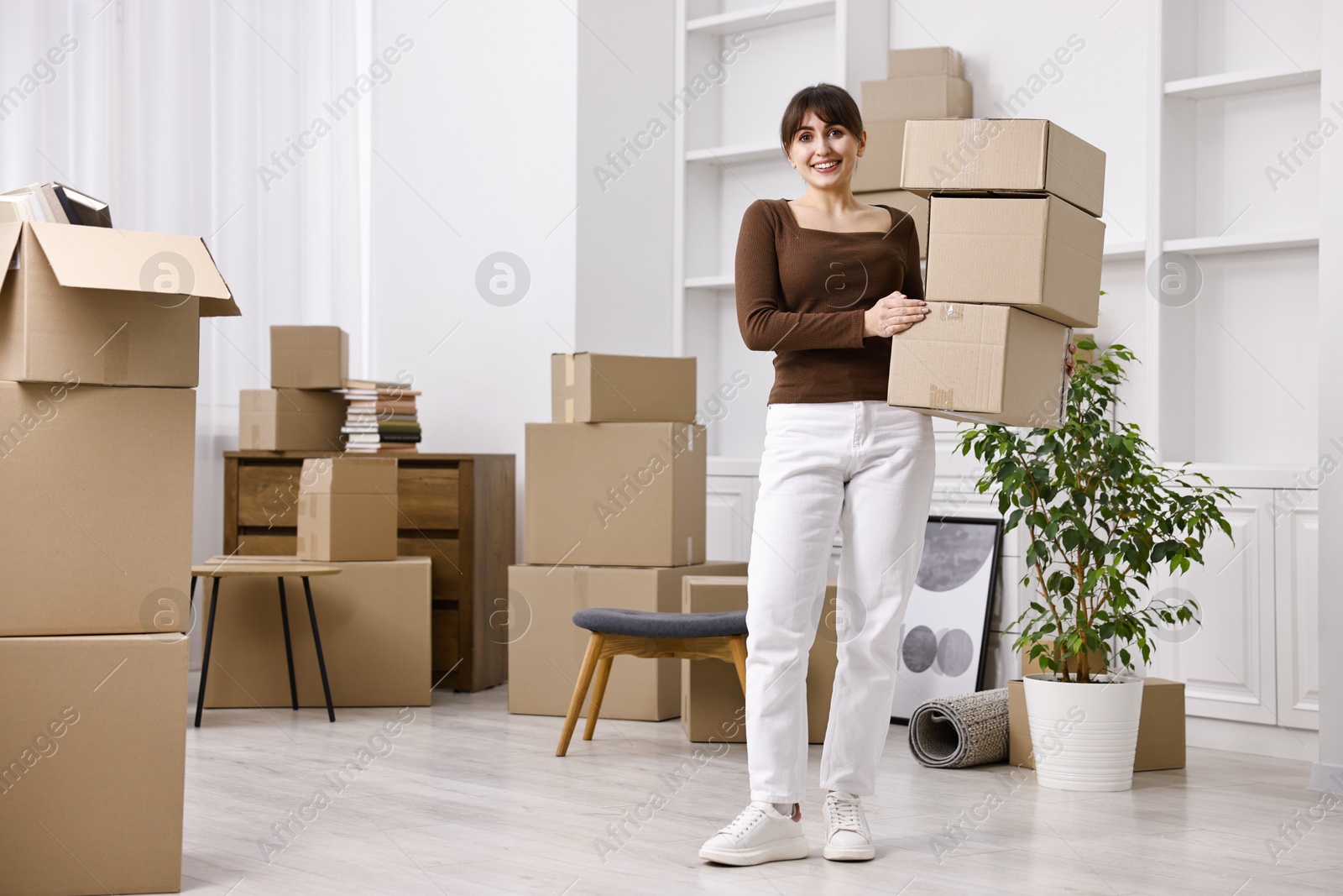 Photo of Moving day. Happy woman with cardboard boxes in her new home