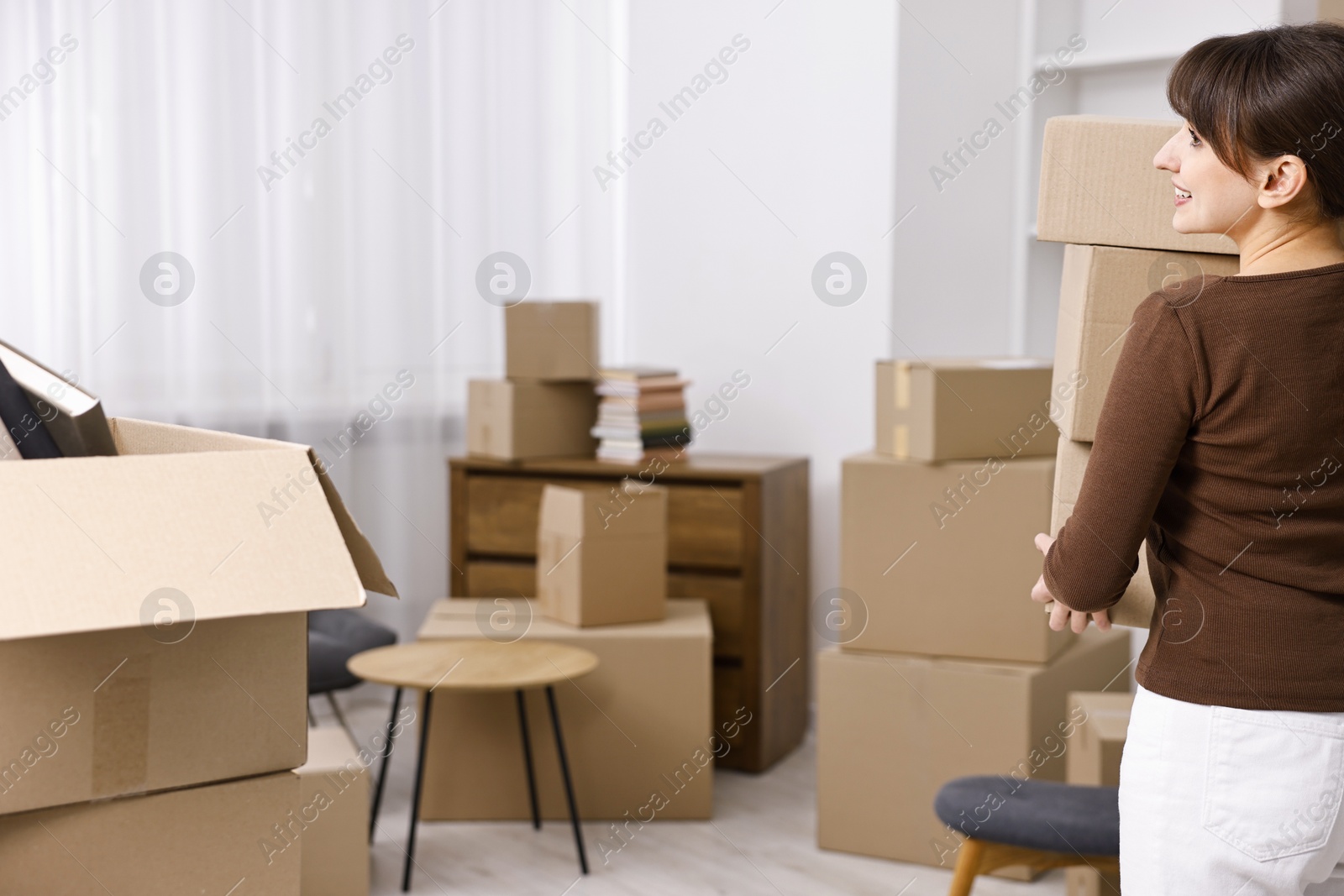 Photo of Moving day. Happy woman with cardboard boxes in her new home