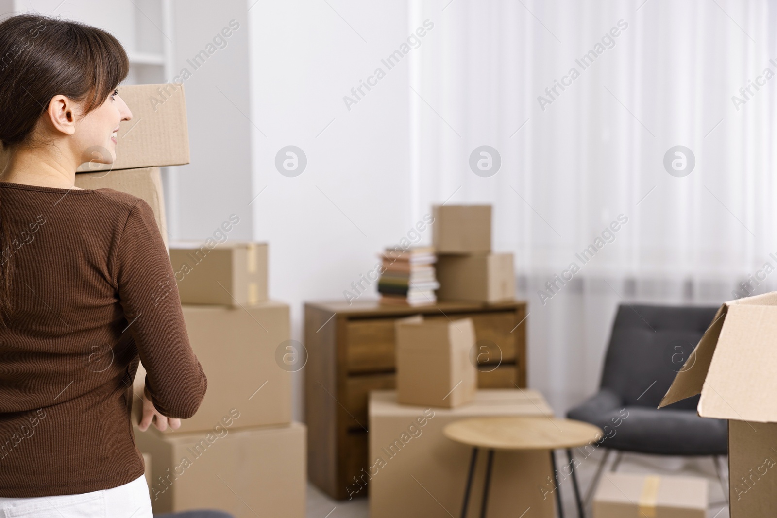 Photo of Moving day. Happy woman with cardboard boxes in her new home