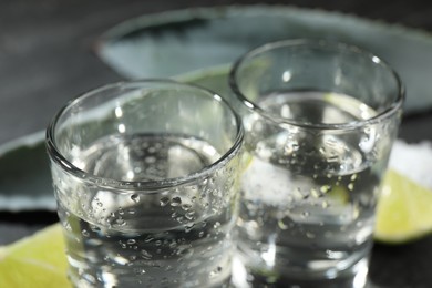 Photo of Tequila in wet shot glasses on blurred background, closeup