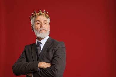 Senior man wearing luxury crown on red background, space for text