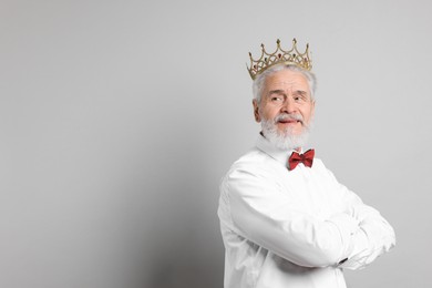 Senior man wearing luxury crown on grey background, space for text