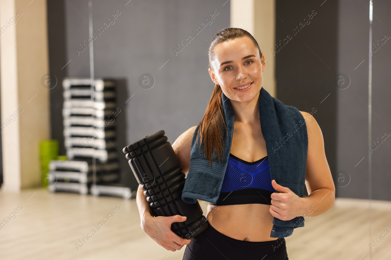 Photo of Happy woman with towel and foam roller in fitness studio