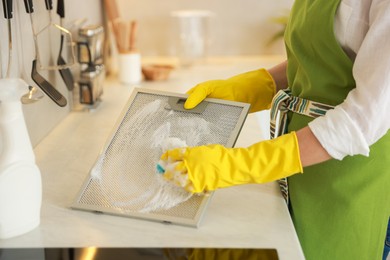 Photo of Woman cleaning filter of kitchen hood with sponge at countertop indoors, closeup