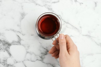 Photo of Woman with glass of tea in metal holder at white marble table, top view