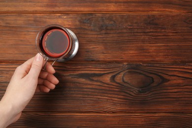 Photo of Woman with glass of tea in metal holder at wooden table, top view. Space for text